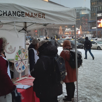 Changemakerin vapaaehtoisia Changemakerin teltalla. Taustalla luminen helsinki.