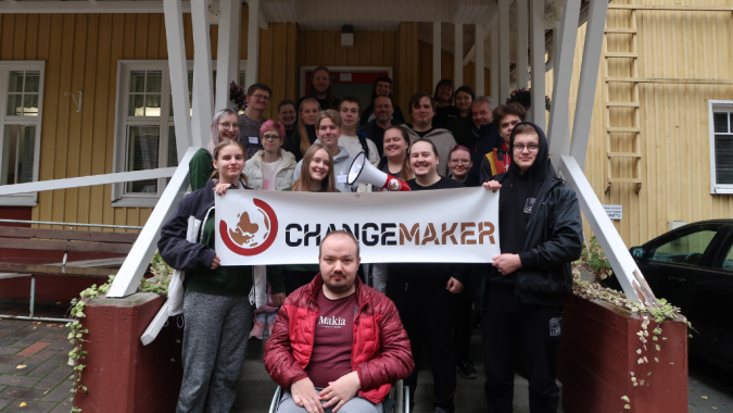 Kuvassa Changemaker-viikonlopun osallistujat leirikeskuksen edessä Changemaker-kyltin kanssa.