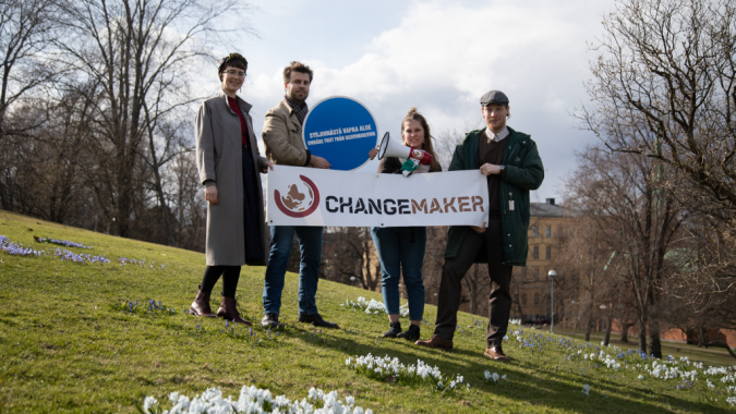 Kuvassa Changemakereitä kukkulalla Changemaker-banderolli ja syrjinnästä vapaa alue -kyltti kädessään.