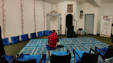 Al-Ghurbaah Foundationin queermoskeijan rukoushuone. Keskellä punapaitainen henkilö istuu lattialla selin kameraan.