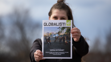 Iida pitää kädessään Globalisti-lehteä ja näyttää sitä kameralle