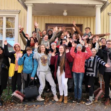 Changemaker-viikonlopun osallistujat seisovat leirikeskuksen edessä ja heiluttavat kameralle