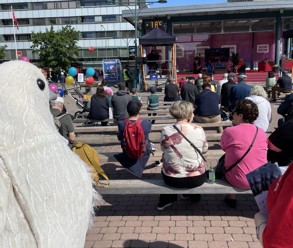Rauhankyyhkypukuun pukeutunut vapaaehtoinen seuraa keskustelutilaisuutta SuomiAreena-tapahtumassa.