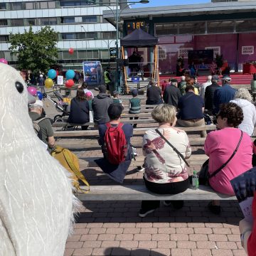 Rauhankyyhkypukuun pukeutunut vapaaehtoinen seuraa keskustelutilaisuutta SuomiAreena-tapahtumassa.