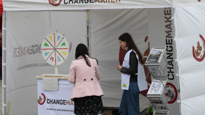 Changemakerin teltalla vapaaehtoinen kertoo ohikulkijalle kampanjasta.