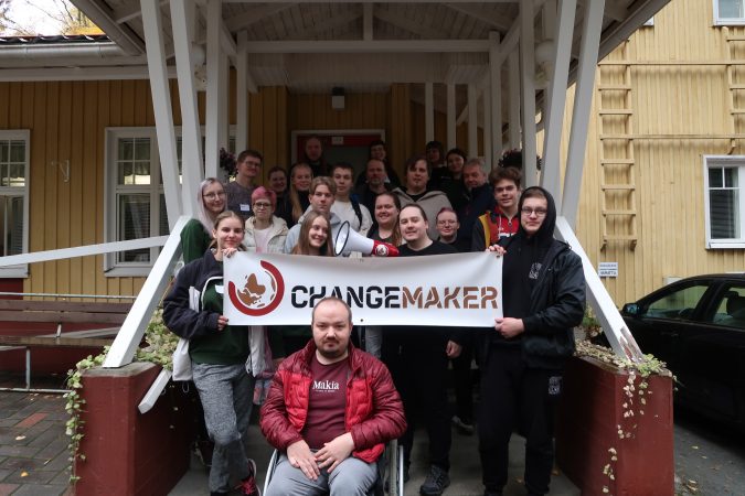 Kuvassa Changemaker-viikonlopun osallistujat leirikeskuksen edessä Changemaker-kyltin kanssa.