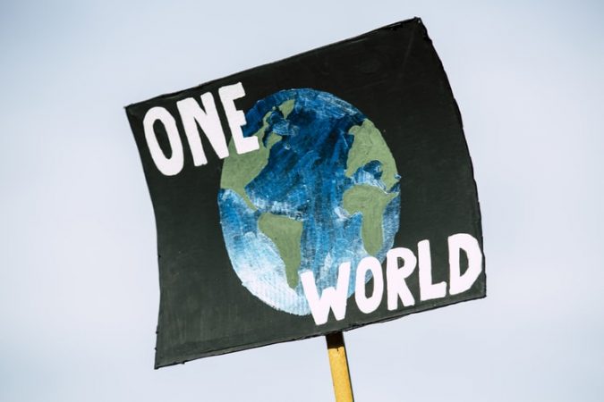 Mielenosoituskyltti, jossa lukee One World ja kuva maapallosta