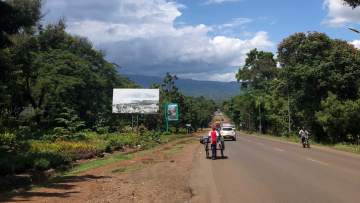 Kuvassa tansanialainen maantie, jossa kulkee autoja ja ihminen kärryn kanssa.
