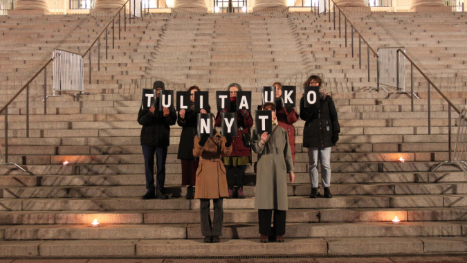 Mielenosoittajia Eduskuntatalon portailla kädessään kylttejä, joista muodostuu sanat "Tulitauko nyt".