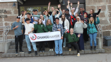 Yhteiskuva Changemaker-viikonlopusta. Nuoret seisovat Nuorisokeskus Anjalan edessä ja pitävät kädessään Changemaker-lakanaa.